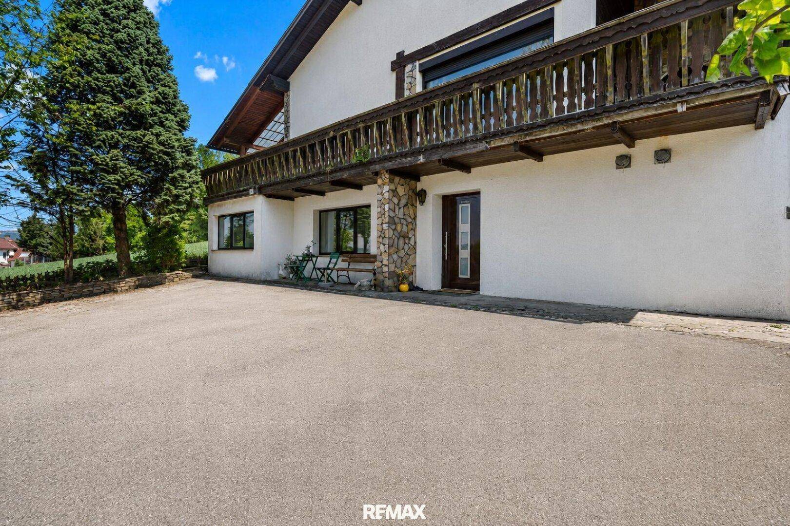 Geräumiges Landhaus mit Balkon und großer gepflasterter Fläche vor dem Eingang.