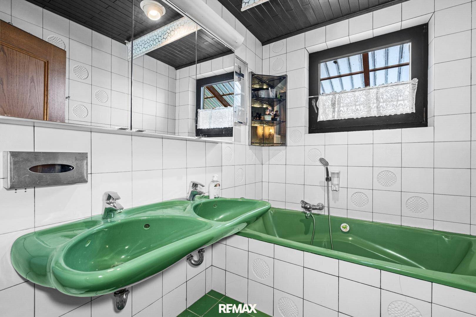 Badezimmer im 80er-Jahre-Stil mit grüner Badewanne, Doppelwaschbecken und weißen Fliesen.