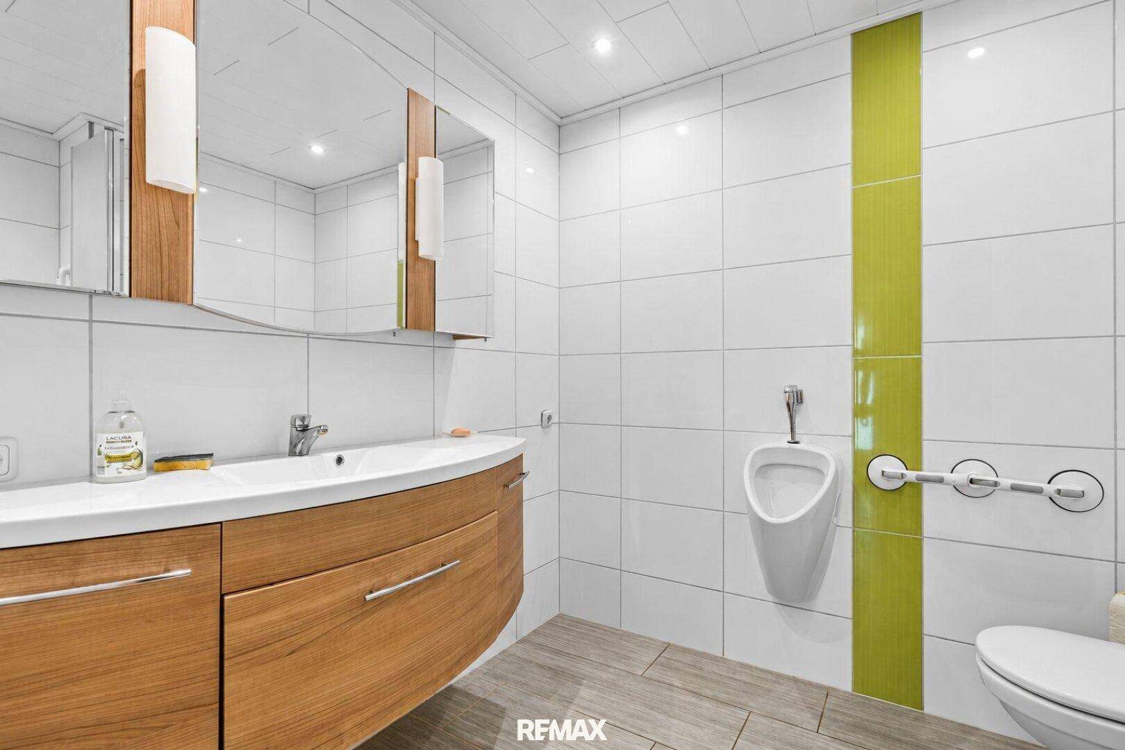 Modernes Badezimmer mit Urinal, Waschtischunterschrank und grünen Akzentfliesen.