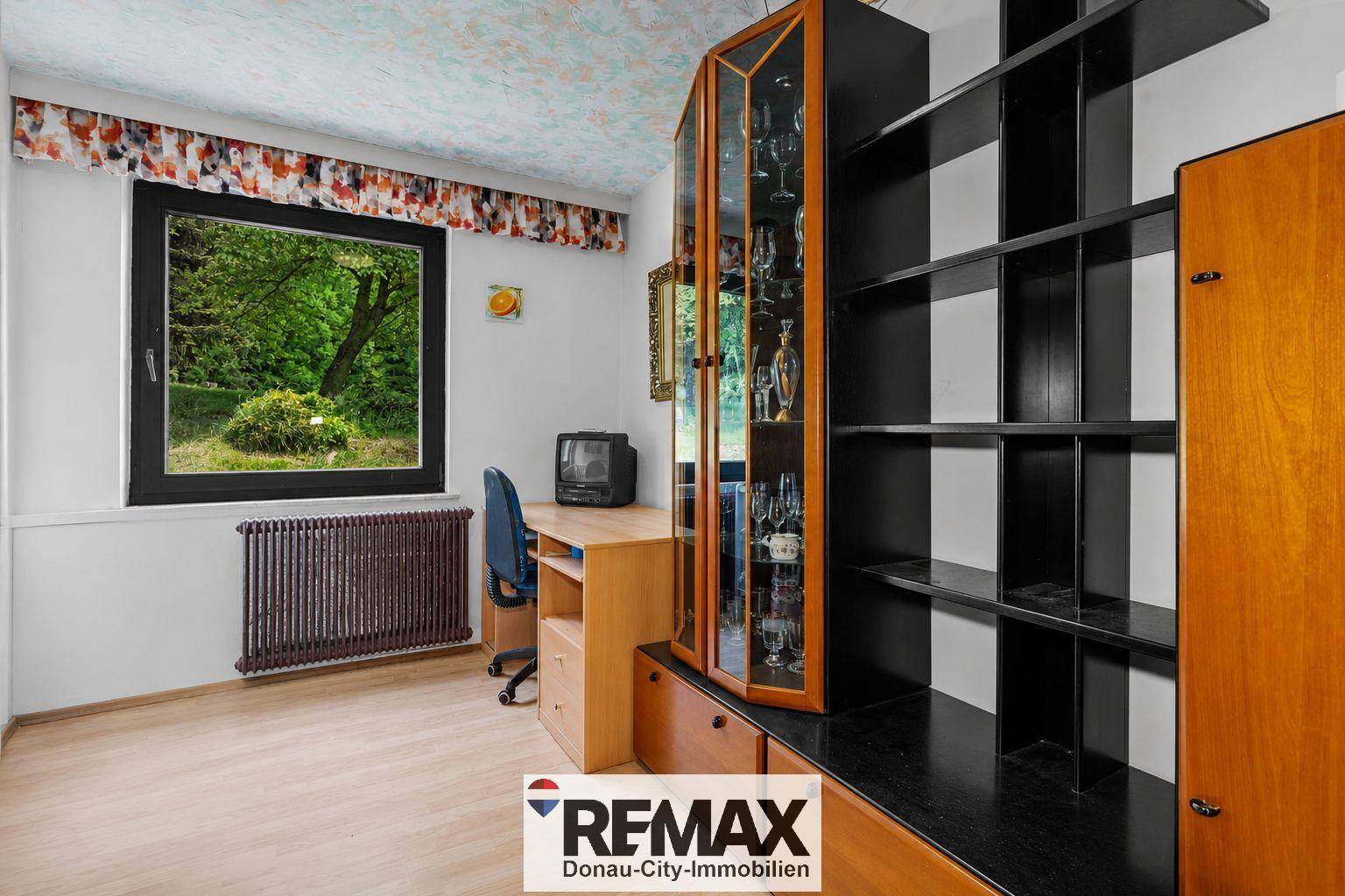 Arbeitszimmer mit Schreibtisch, Bücherregal und Fenster mit Blick ins Grüne.