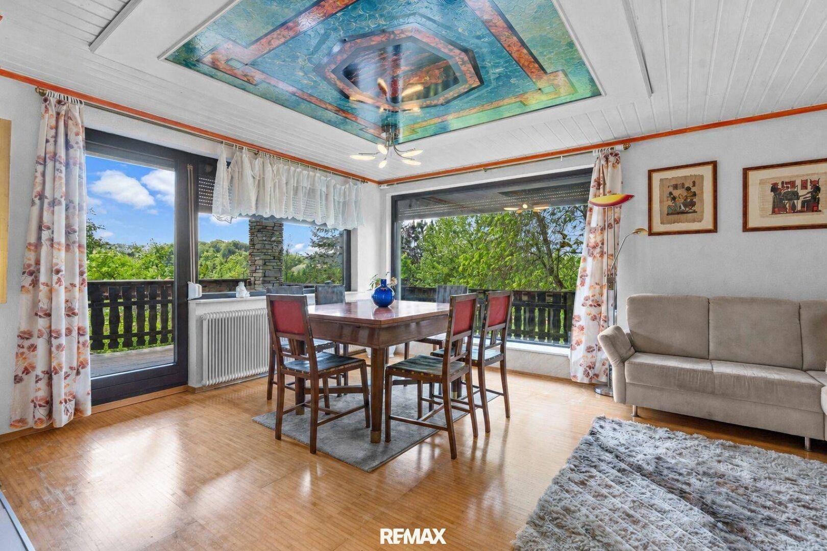 Heller Wohn- und Essbereich mit Holzboden, Deckenmalerei und Zugang zum Balkon.