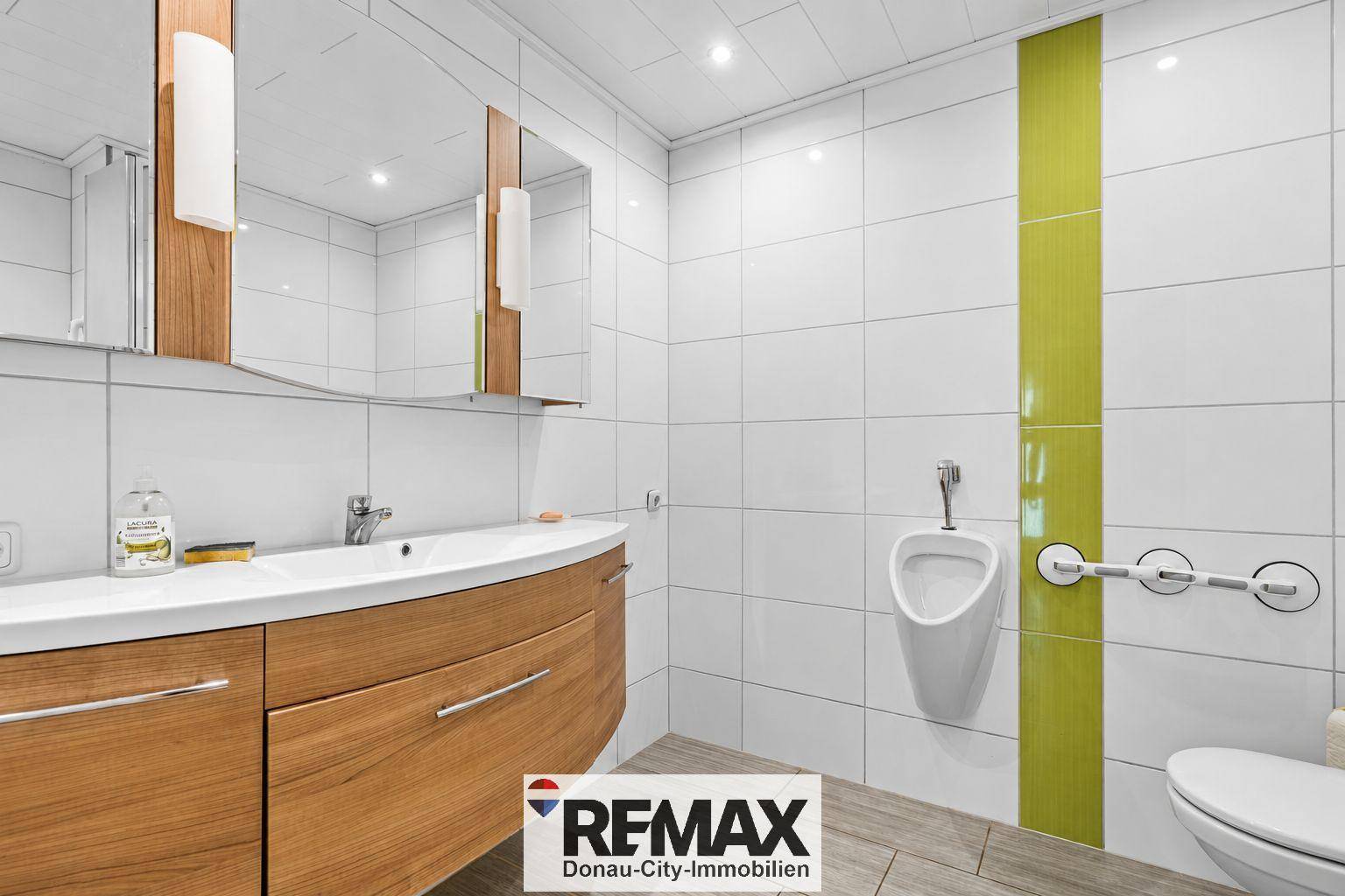 Modernes Badezimmer mit Waschtisch, Urinal, WC und grünen Akzentfliesen.