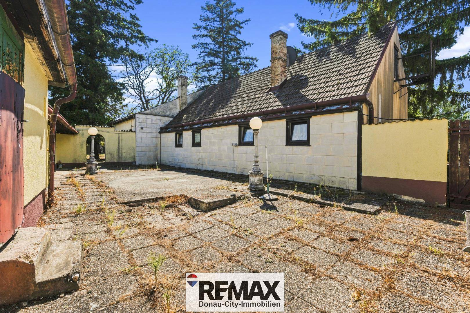 Gepflasterter Seitenbereich des Hauses mit Fenstern und traditionellem Schornstein.