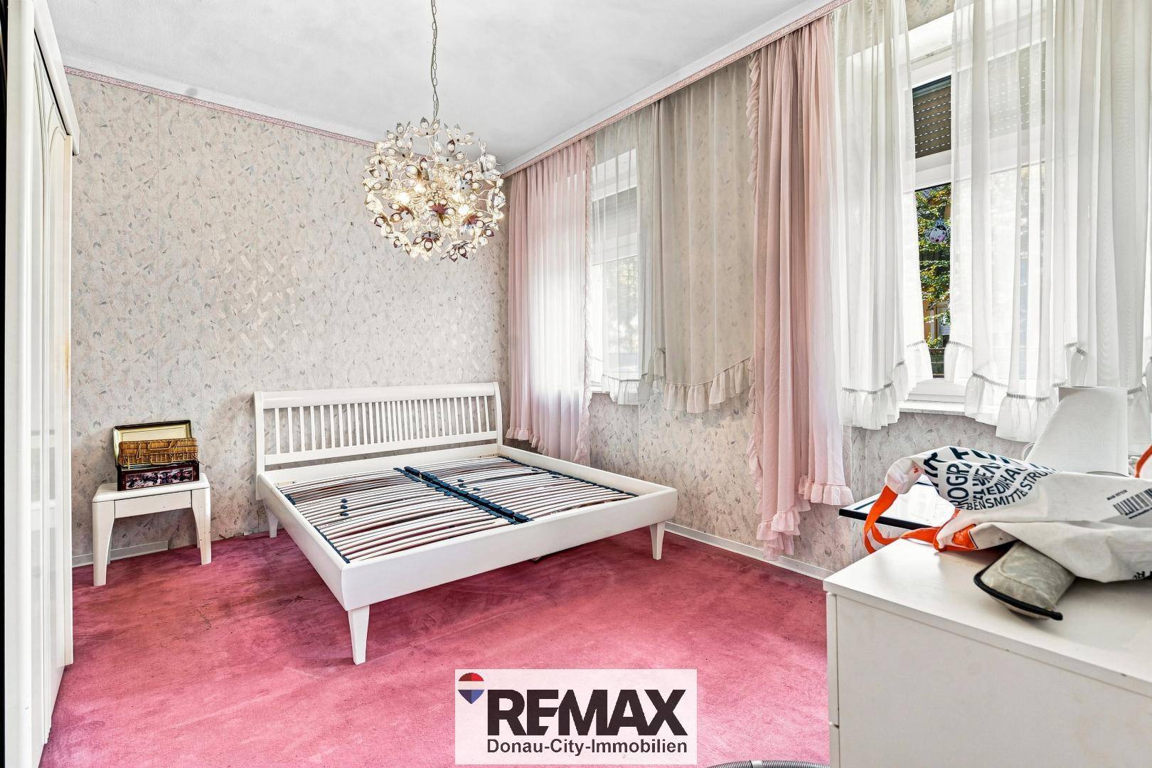 Schlafzimmer mit weißem Bettrahmen, rosa Teppichboden und eleganten Vorhängen.