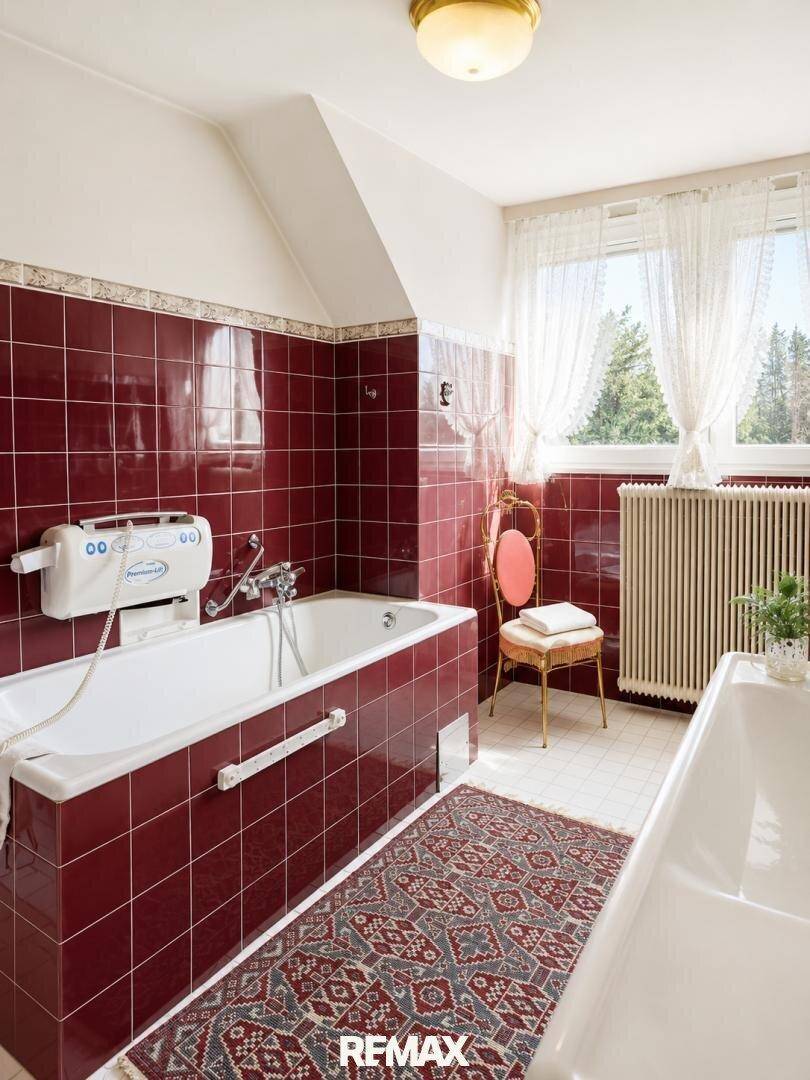 Klassisches Badezimmer mit roten Fliesen, Badewanne und Fenster mit Blick ins Grüne.