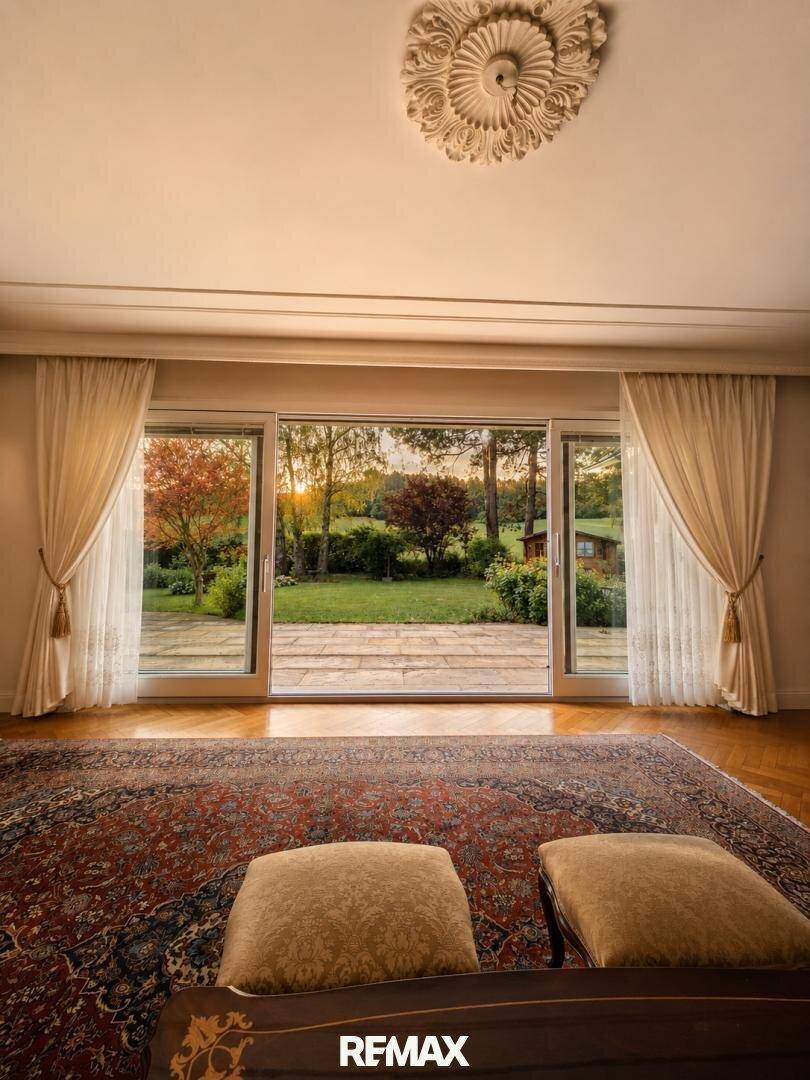 Gemütliches Wohnzimmer mit Teppich, Blick auf den Garten und dekorativer Stuckdecke.