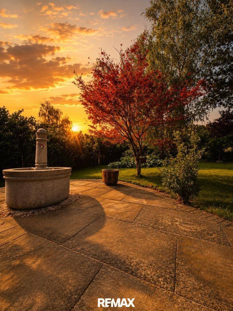 Sonniger Terrassenbereich mit Steinplatten, einem dekorativen Brunnen und Blick in den Garten.