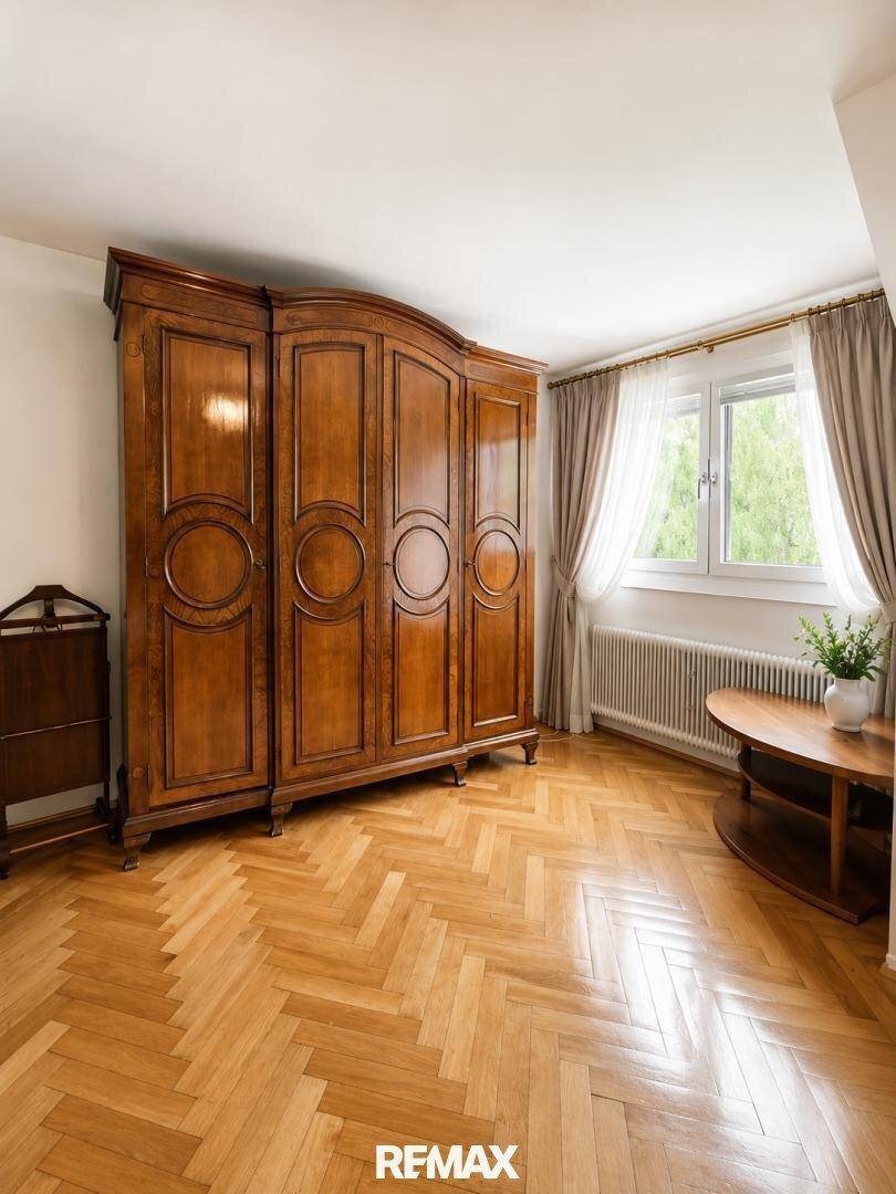 Geräumiges Schlafzimmer mit Fischgrätparkett, großem Holzschrank und Fenster mit Blick ins Grüne.