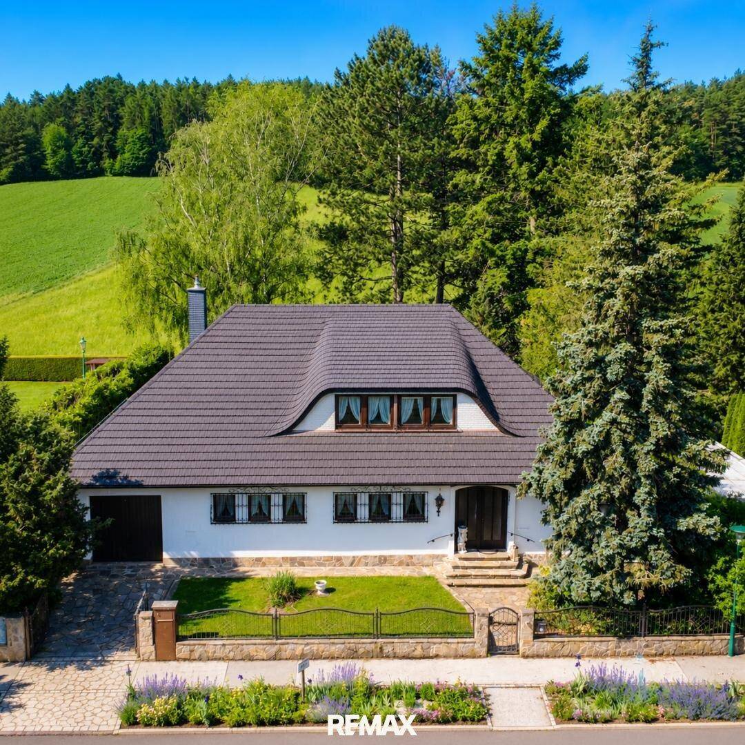 Charmantes Einfamilienhaus mit gepflegtem Vorgarten und Blick auf die umliegende grüne Landschaft.