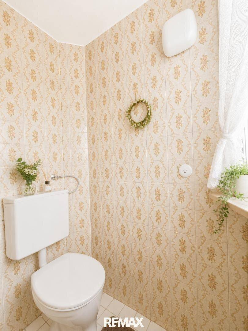 Separate Toilette mit gemusterten Fliesen und kleinem Fenster für Tageslicht.