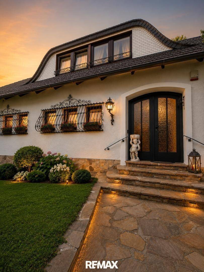 Eingangsbereich des Hauses bei Sonnenuntergang mit beleuchtetem Weg und dekorativen Elementen.