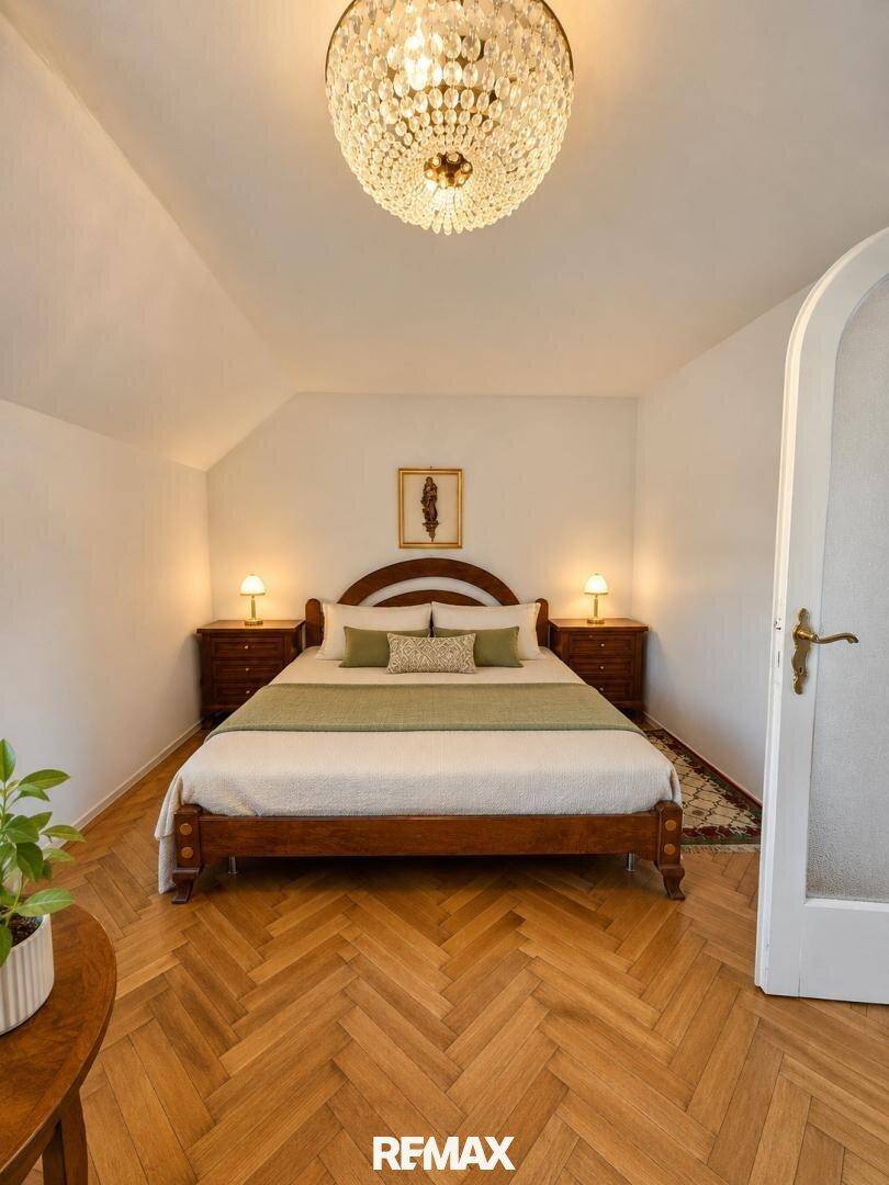 Helles Schlafzimmer mit Fischgrätparkett, Holzbett und einem eleganten Kronleuchter.