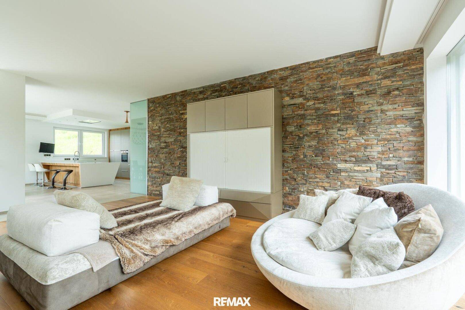 Modernes Wohnzimmer mit Holzboden, Steinwand und bequemen Sitzmöbeln.