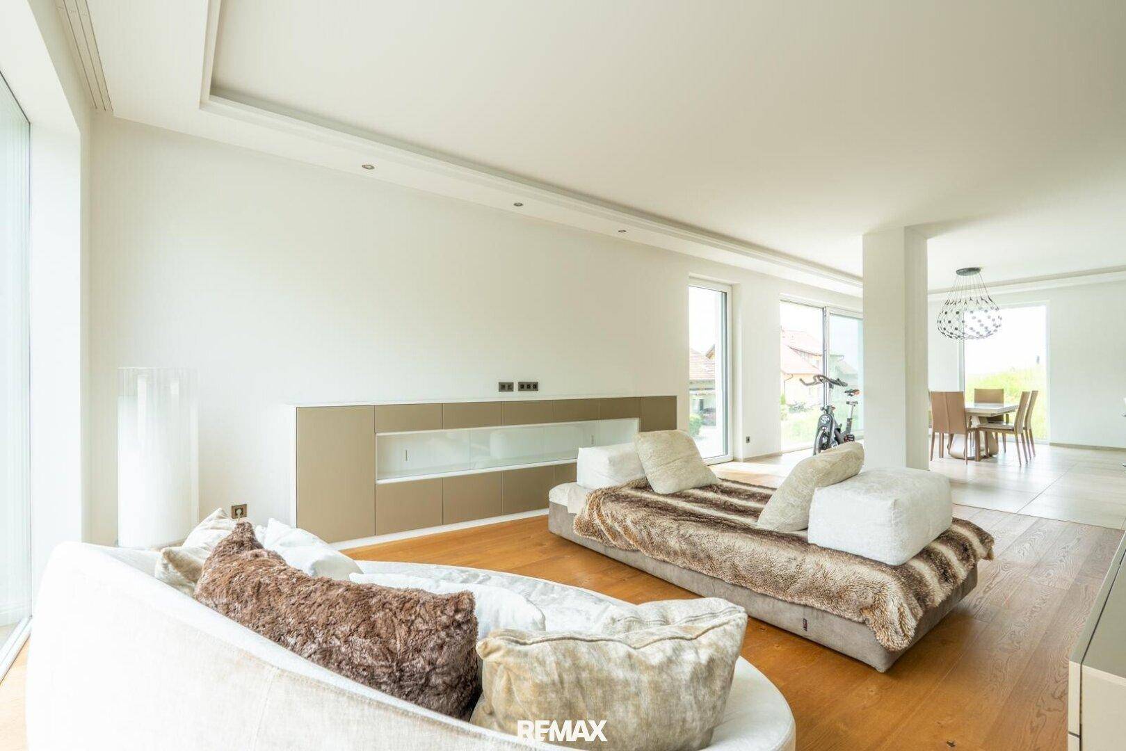 Geräumiges Wohnzimmer mit Holzboden, großen Fenstern und Blick in den Essbereich.