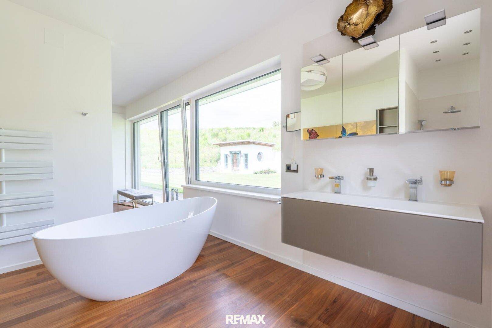 Modernes Badezimmer mit freistehender Badewanne, Doppelwaschbecken und großen Fenstern.