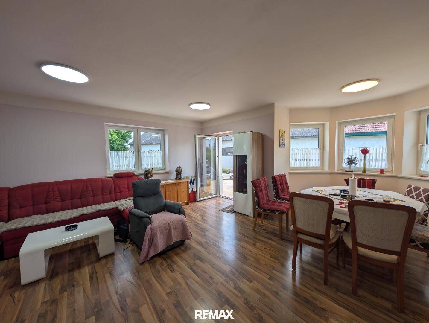 Geräumiger Wohn-Essbereich mit Laminatboden, rotem Sofa und Zugang zur Terrasse.
