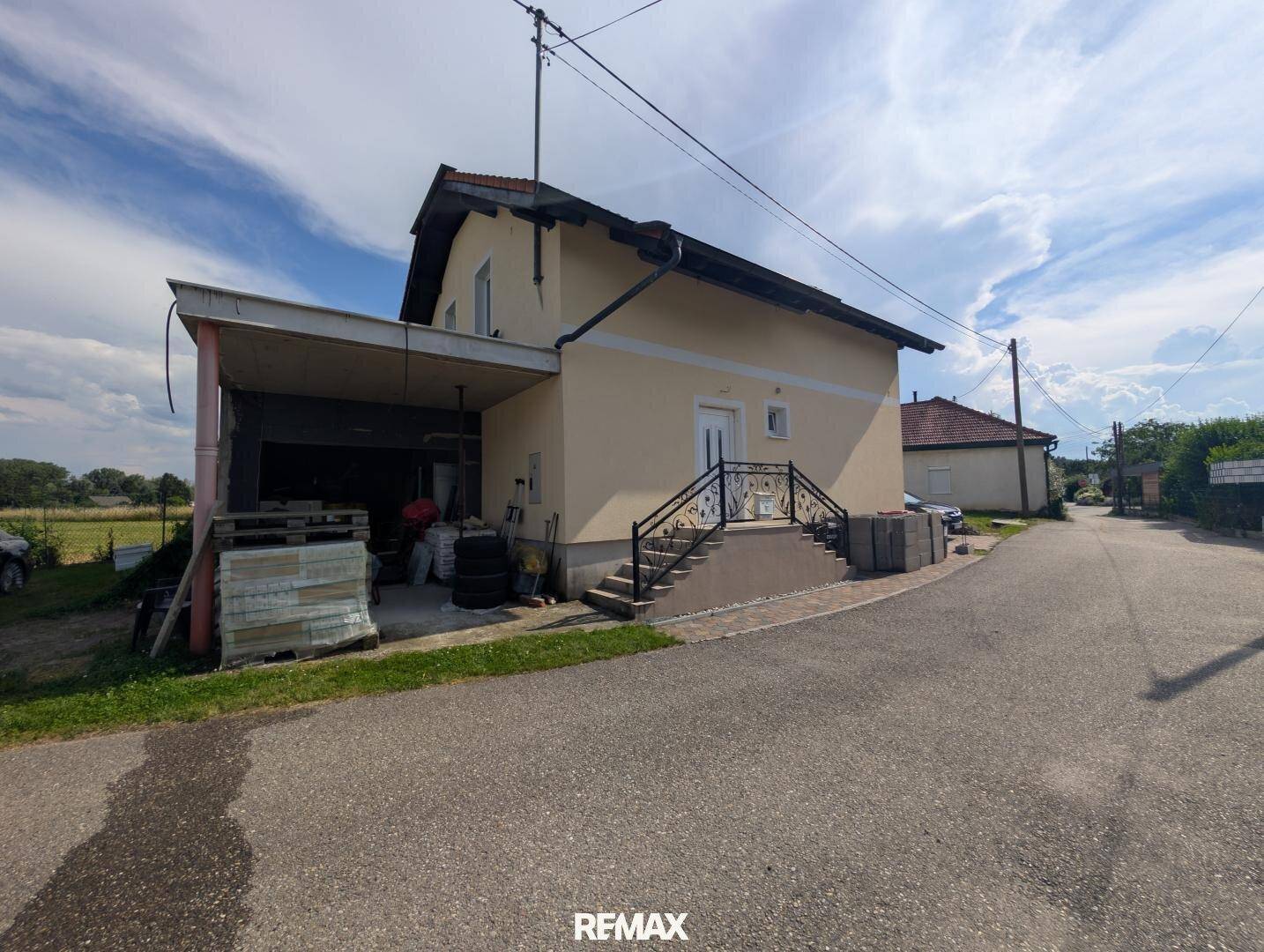 Einfamilienhaus mit Carport und Zufahrt, umgeben von ländlicher Landschaft.