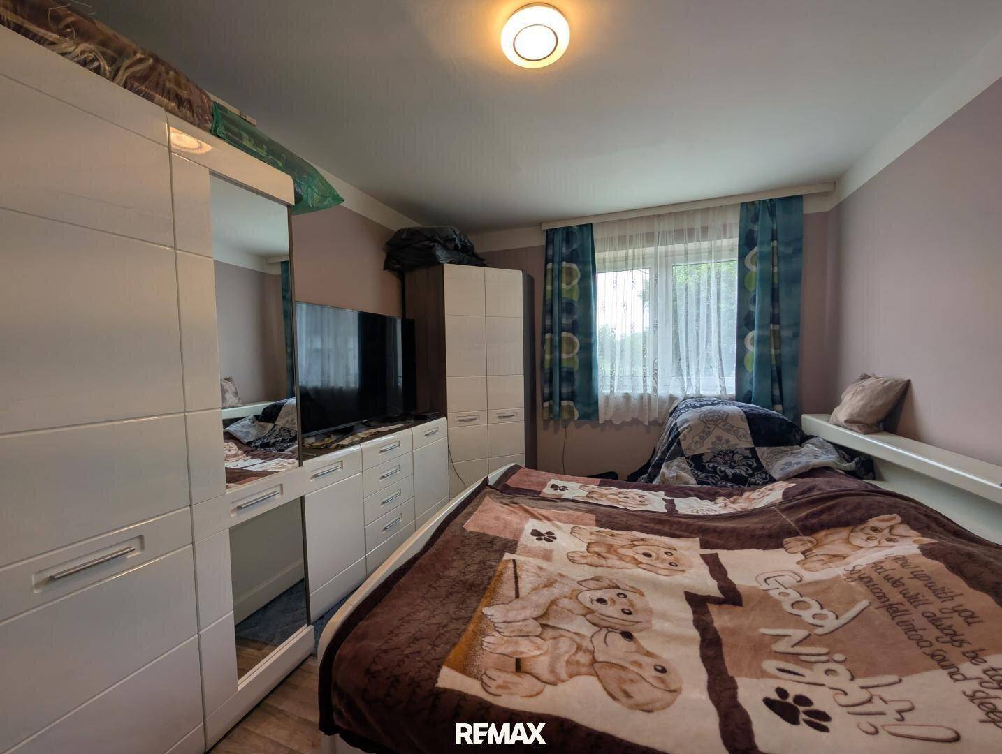 Schlafzimmer mit Bett, weißen Kleiderschränken und Fenster mit blauen Vorhängen.