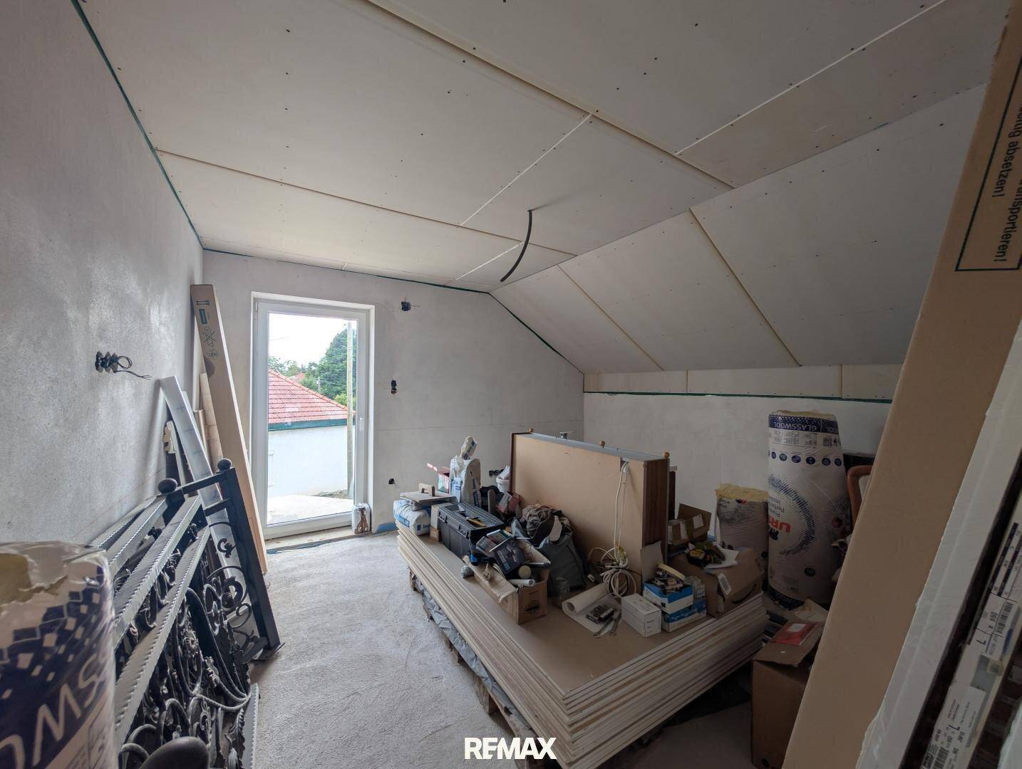Dachgeschossraum im Rohbau mit Trockenbauwänden und Baumaterialien.