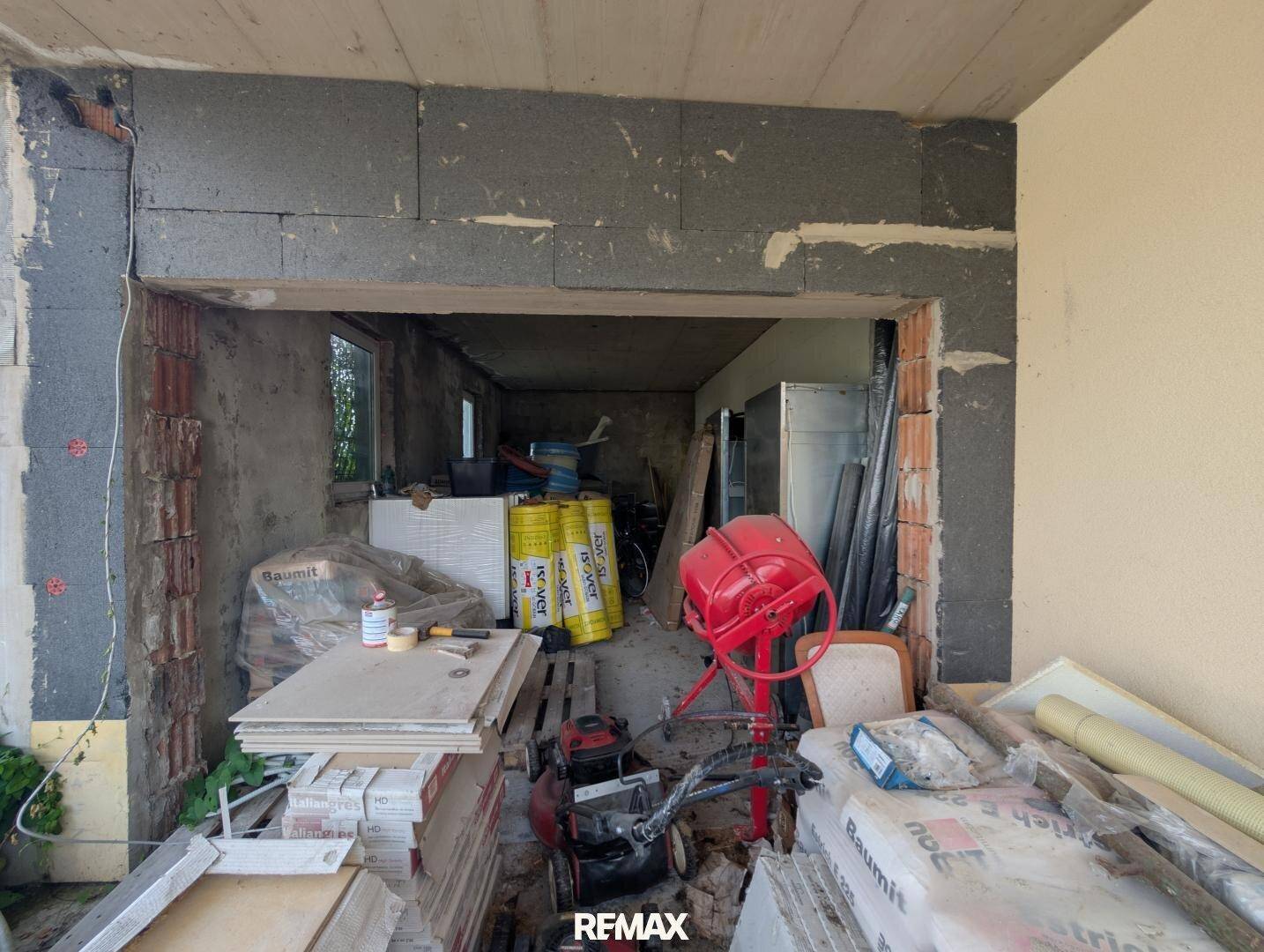 Innenraum im Rohbau mit Baumaterialien und sichtbarer Isolierung.