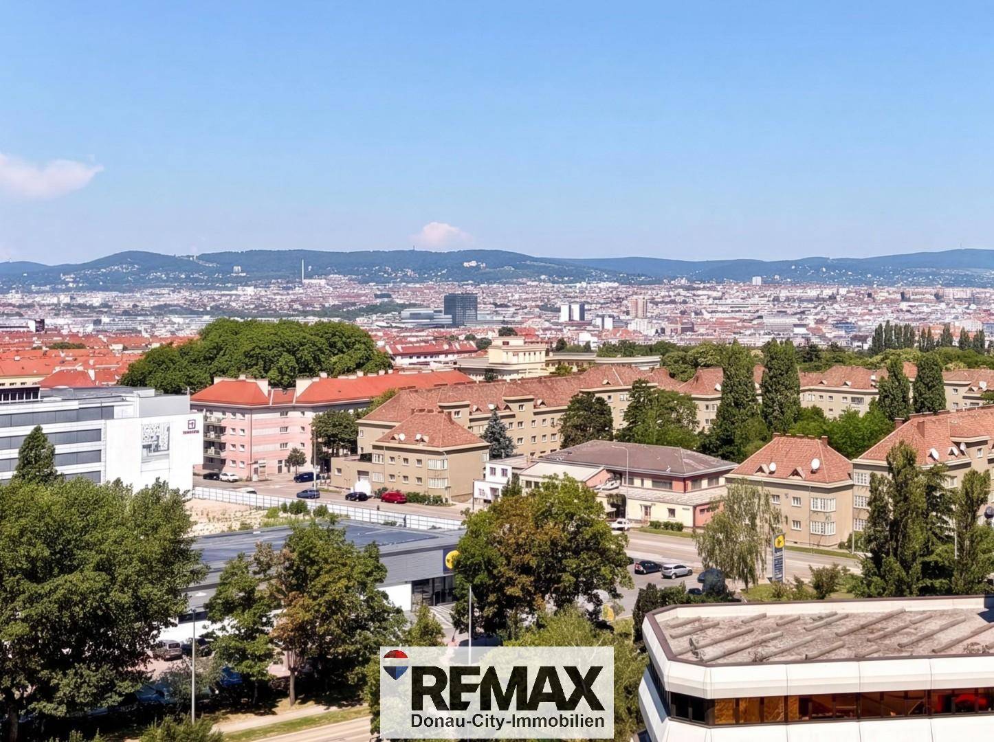 Panoramablick über die Stadt Wien mit Hügeln im Hintergrund an einem sonnigen Tag.