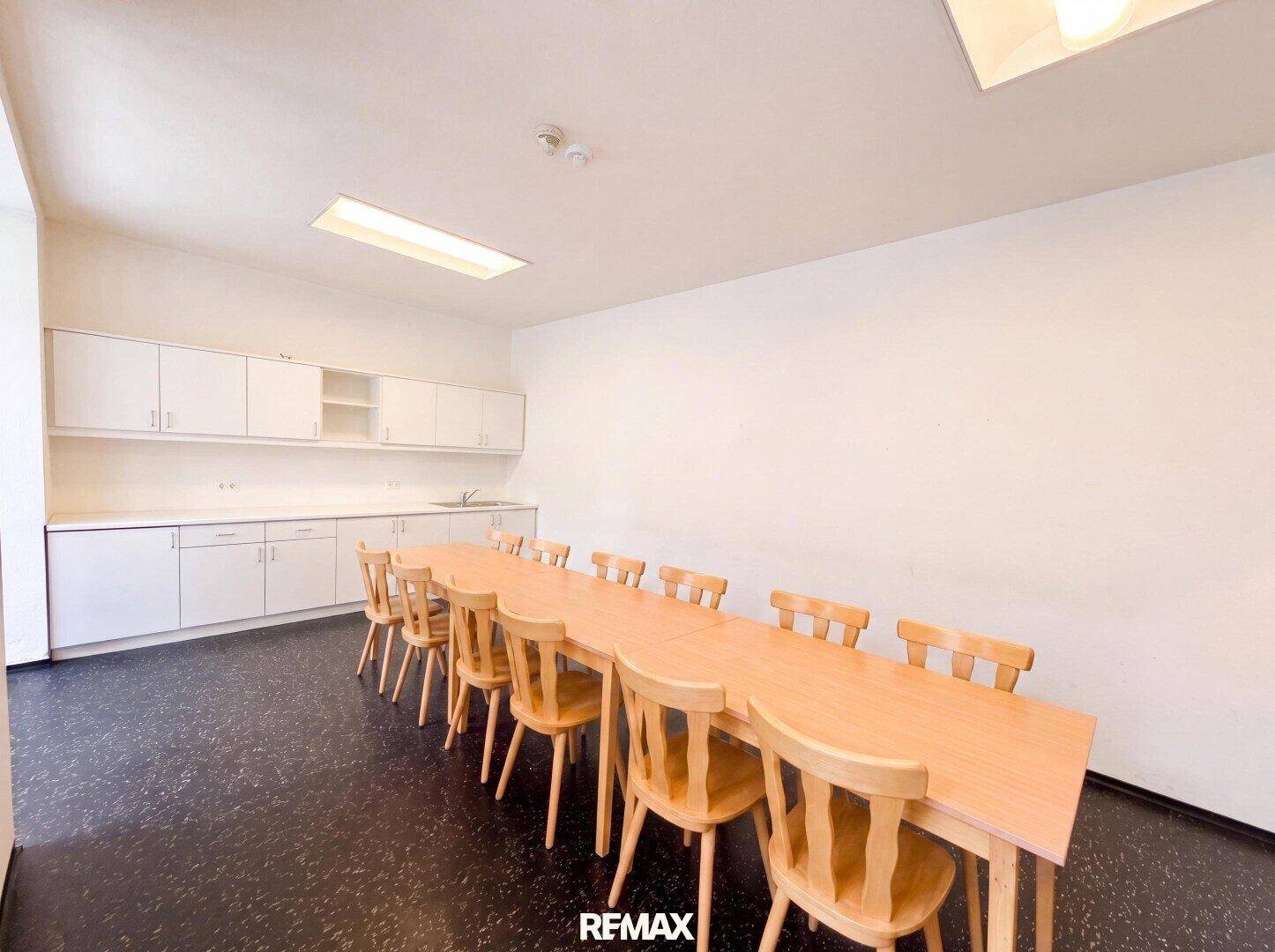 Großer Gemeinschaftsraum mit langer Holztafel, Stühlen und einer Küchenzeile.