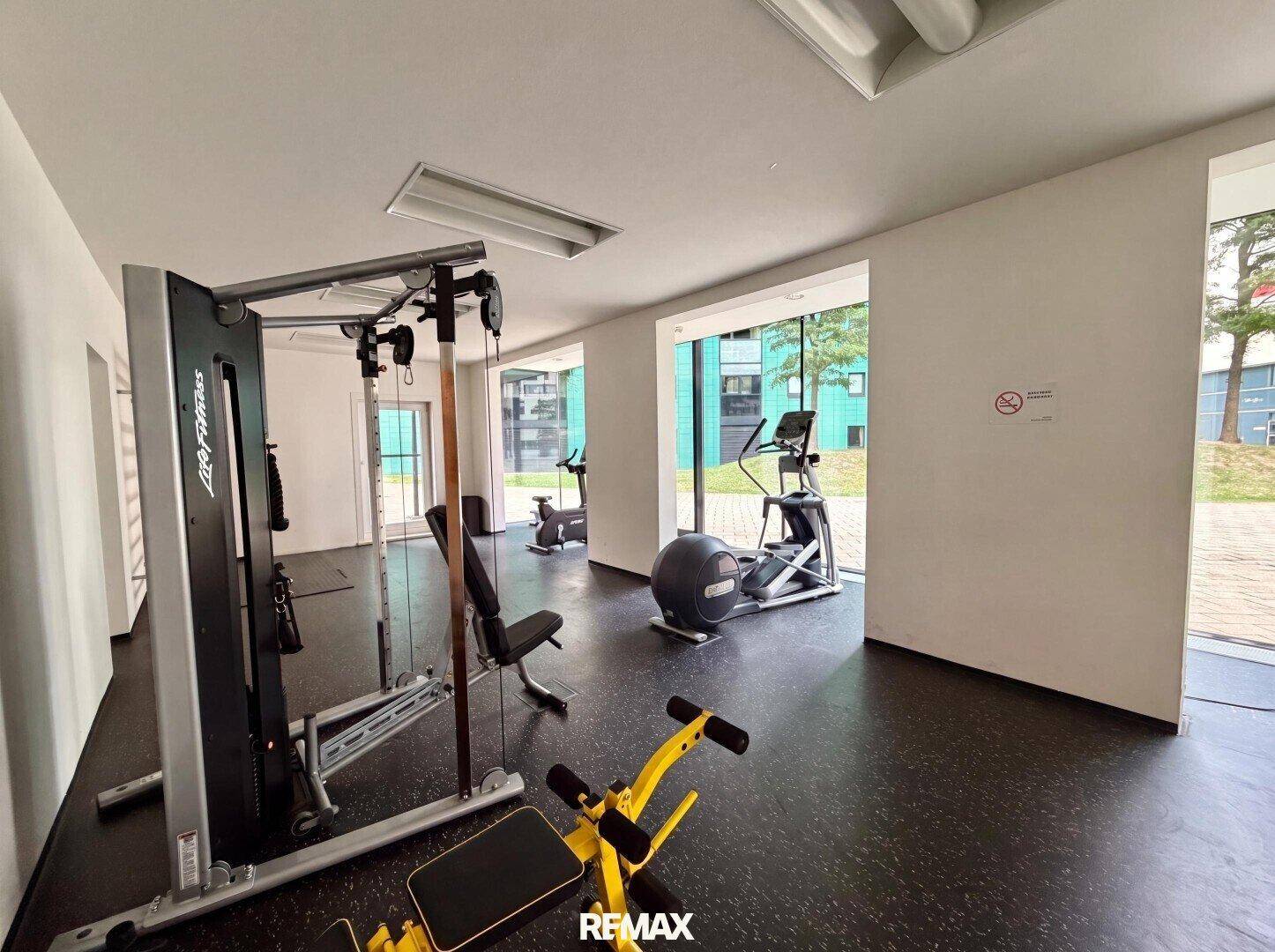Gut ausgestatteter Fitnessraum mit verschiedenen Trainingsgeräten und großen Fenstern.