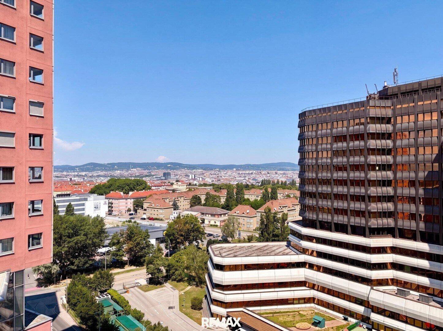 Panoramablick auf eine städtische Skyline mit verschiedenen Gebäuden und grünen Hügeln im Hintergrund.