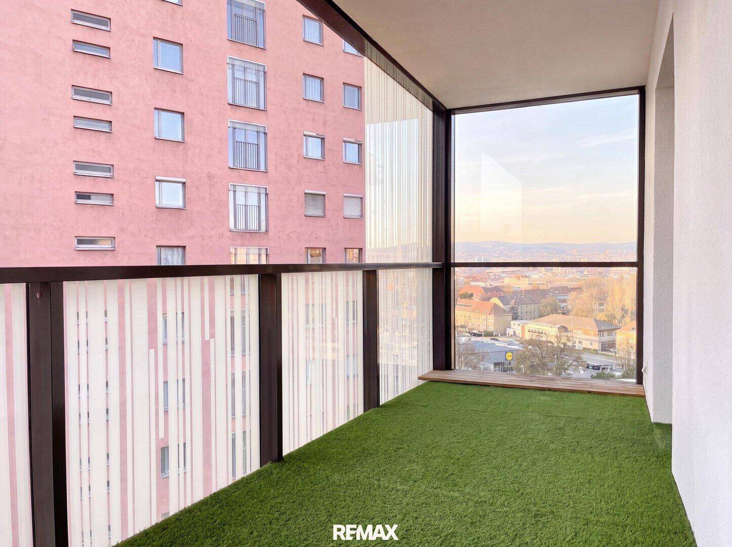 Moderner Balkon mit Kunstrasen und Glasbrüstung, bietet einen weiten Blick über die Stadt.