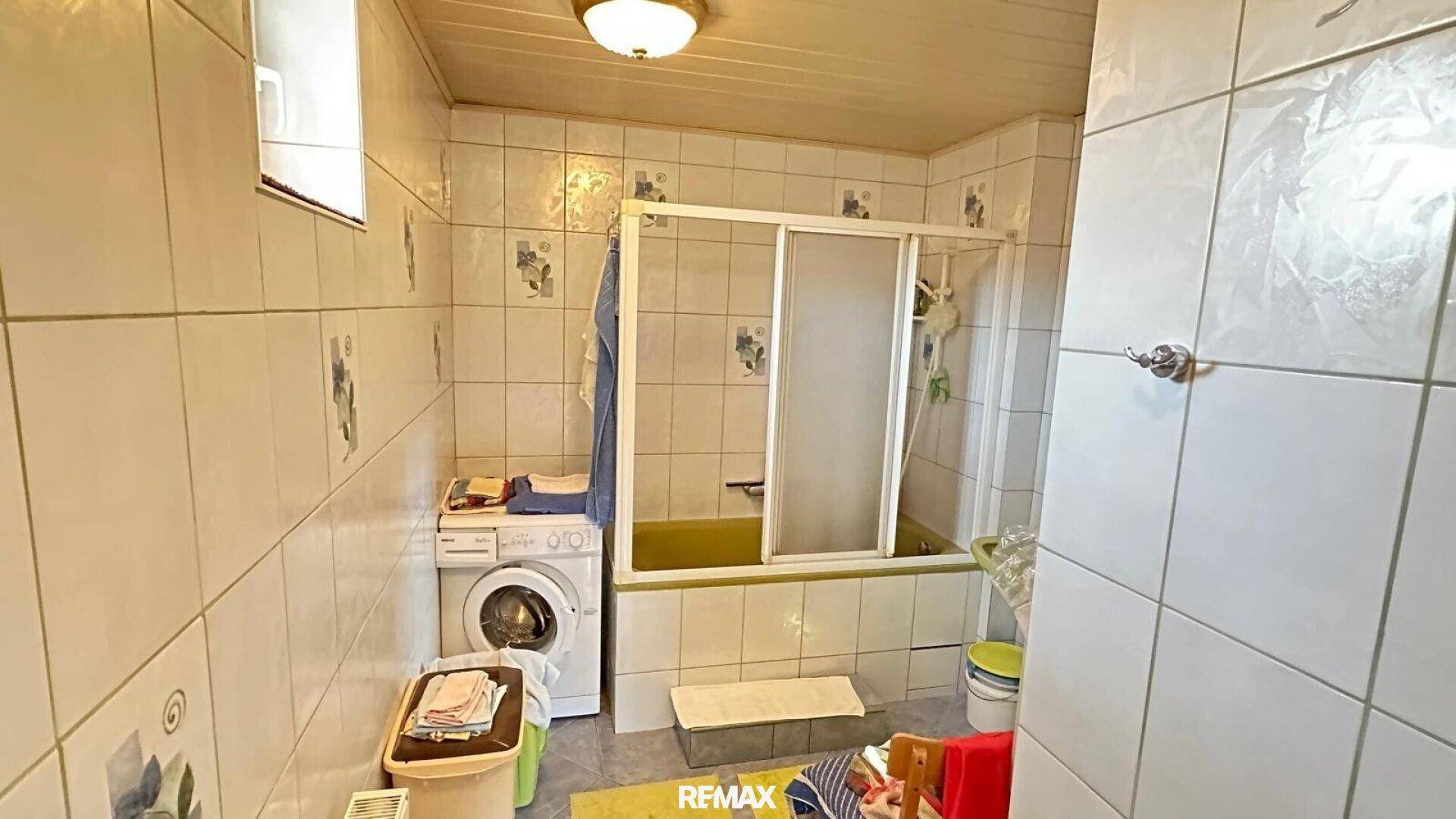 Badezimmer mit Badewanne, Duschabtrennung und Waschmaschine, komplett gefliest.