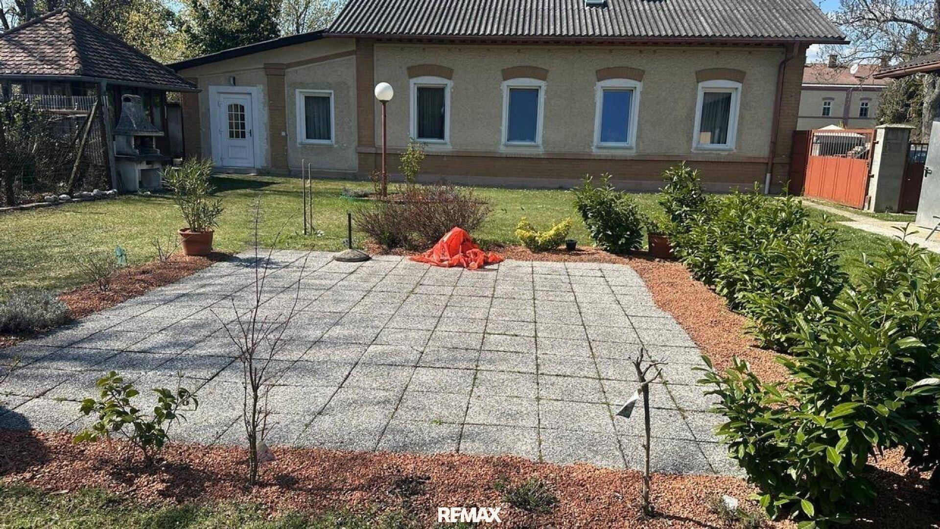 Gepflasterte Terrasse im Garten, umgeben von Sträuchern und Beeten.