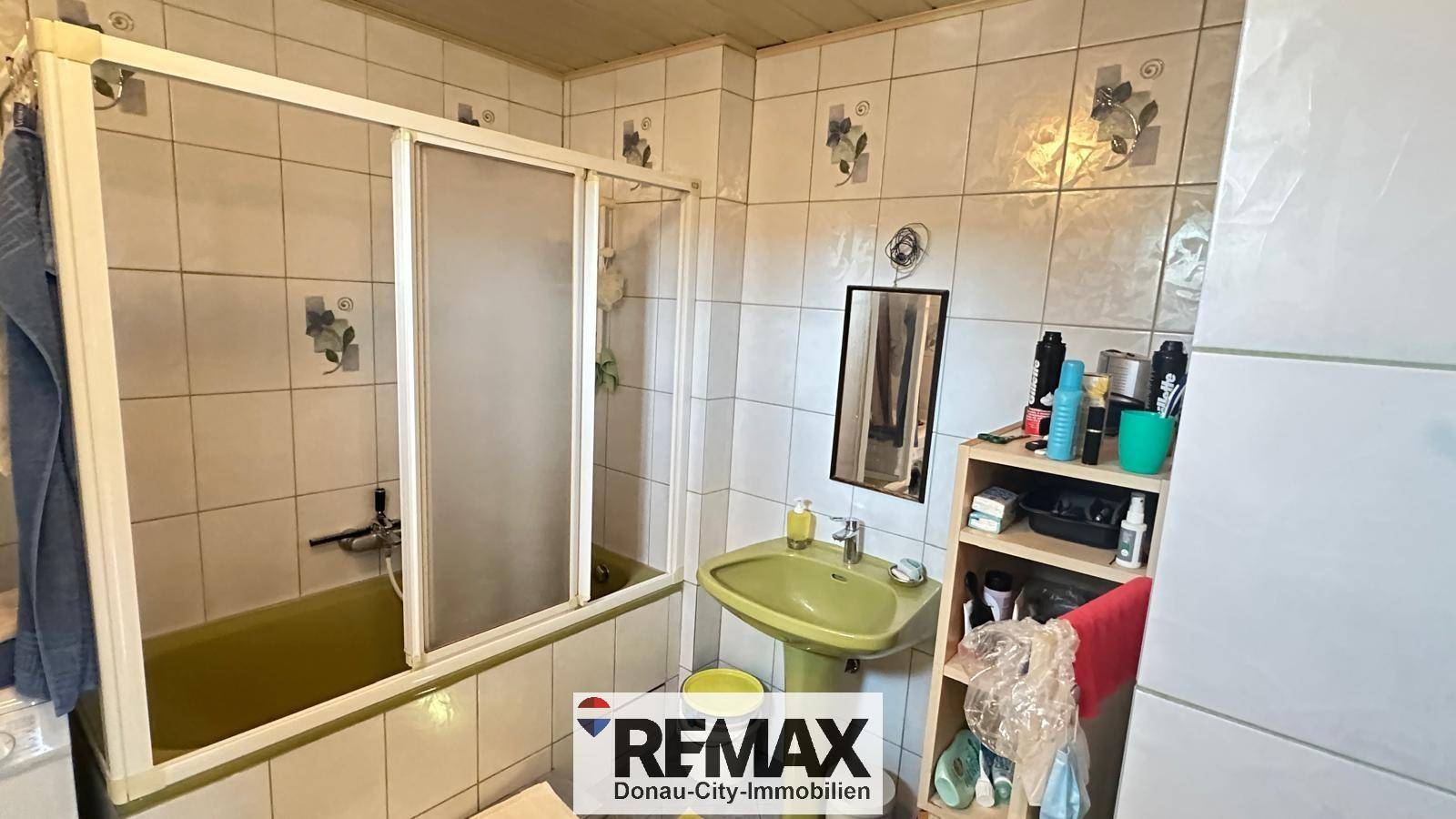 Badezimmer mit Fliesen, Badewanne mit Duschabtrennung und einem einzelnen Waschbecken.