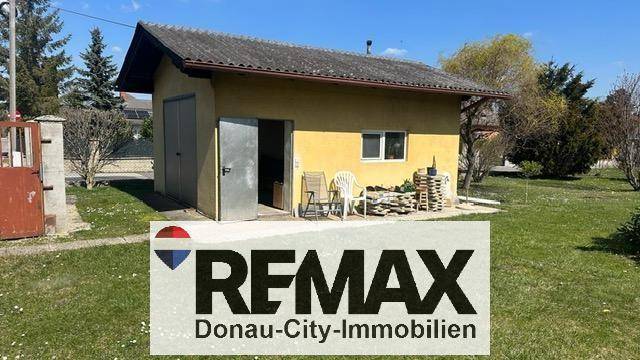 Nebengebäude oder Garage mit offenem Tor und Sitzgelegenheiten im Grünen.