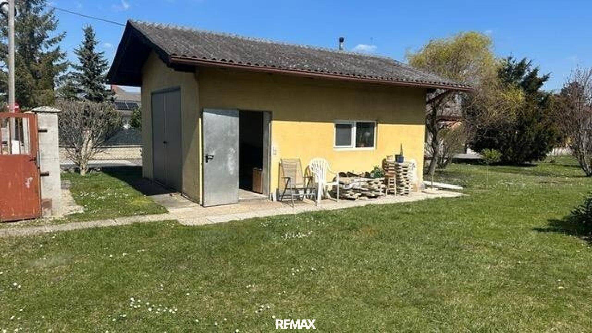 Freistehende Garage mit Schuppen und kleinem gepflasterten Bereich im Garten.