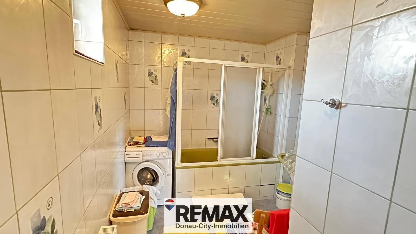 Badezimmer mit Fliesen, Badewanne mit Duschabtrennung und integrierter Waschmaschine.