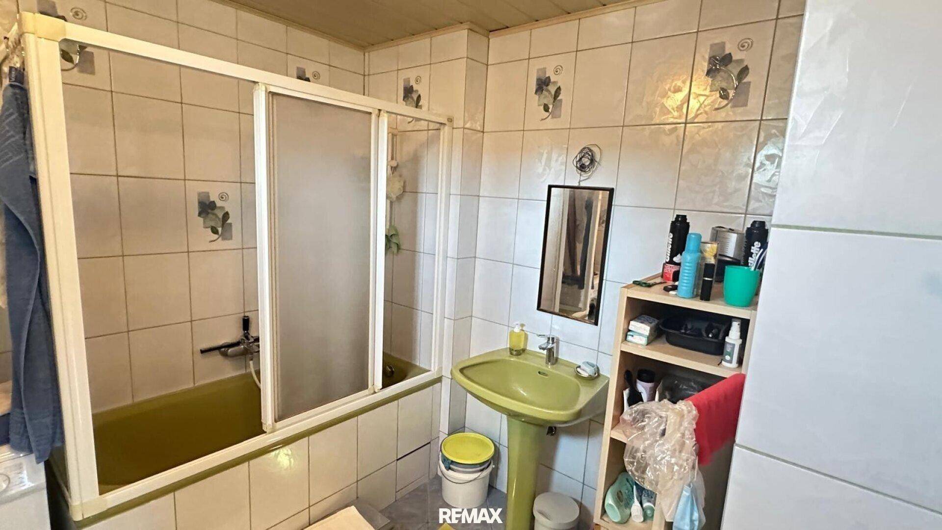 Gefliestes Badezimmer mit Badewanne, Duschabtrennung und grünem Waschbecken.