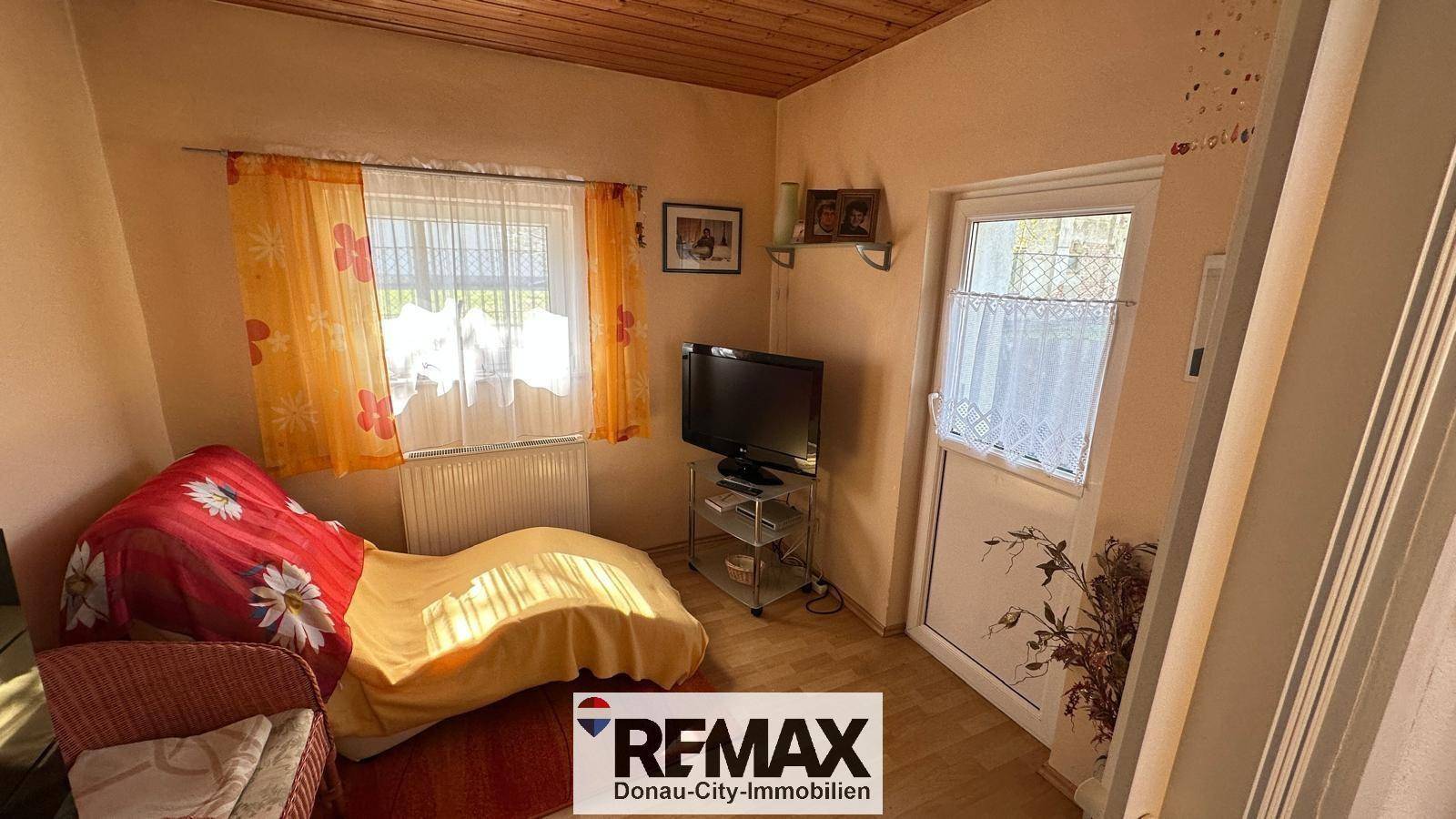 Kleines Schlafzimmer mit Holzboden, Fenster und einem Fernseher, einfach eingerichtet.