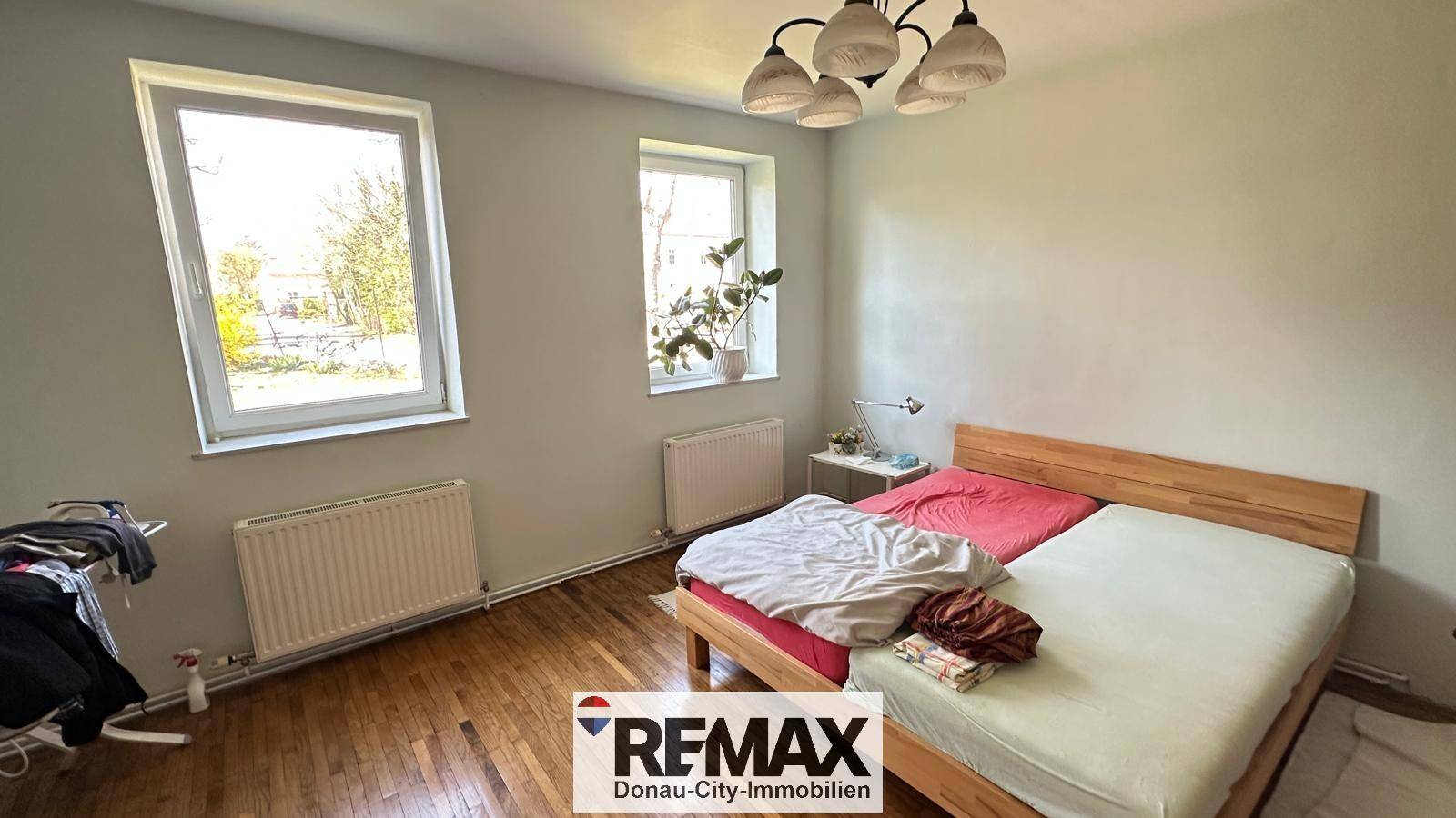Helles Schlafzimmer mit Holzbett und zwei Fenstern, die viel natürliches Licht hereinlassen.