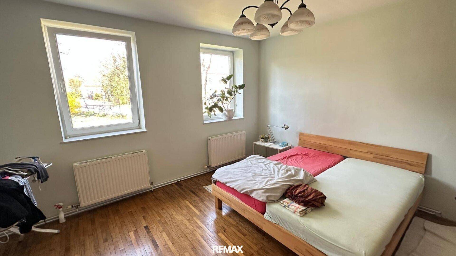 Helles Schlafzimmer mit Holzfußboden, Doppelbett und zwei Fenstern.