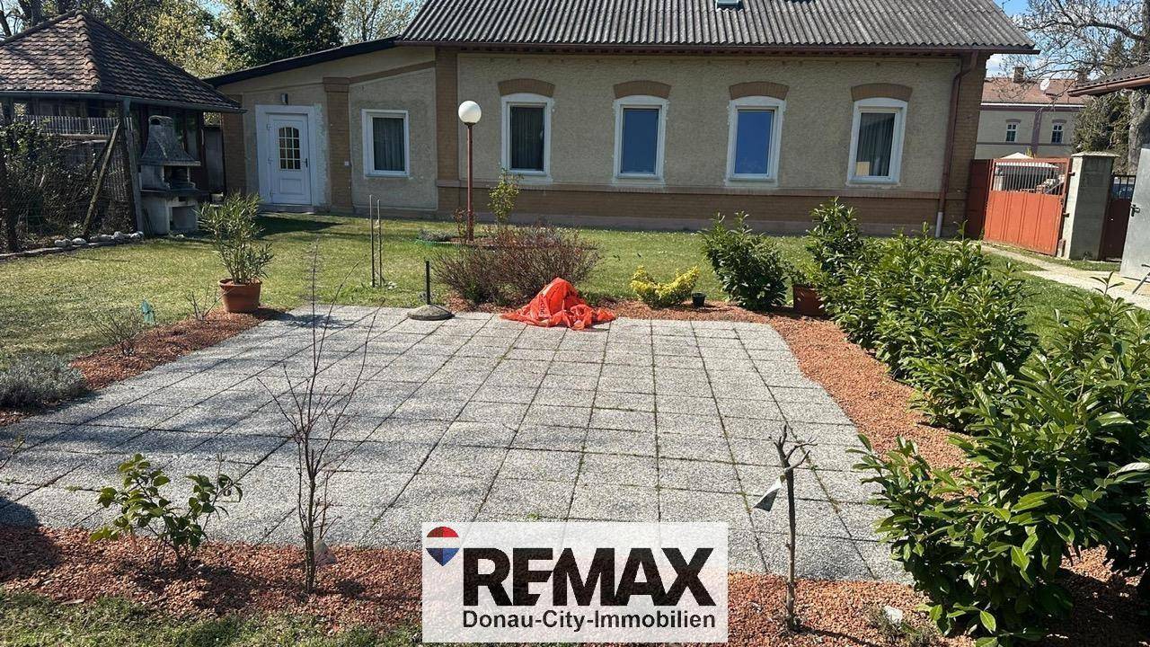 Gepflasterte Terrasse im Gartenbereich eines Hauses mit Rasenfläche und Sträuchern.