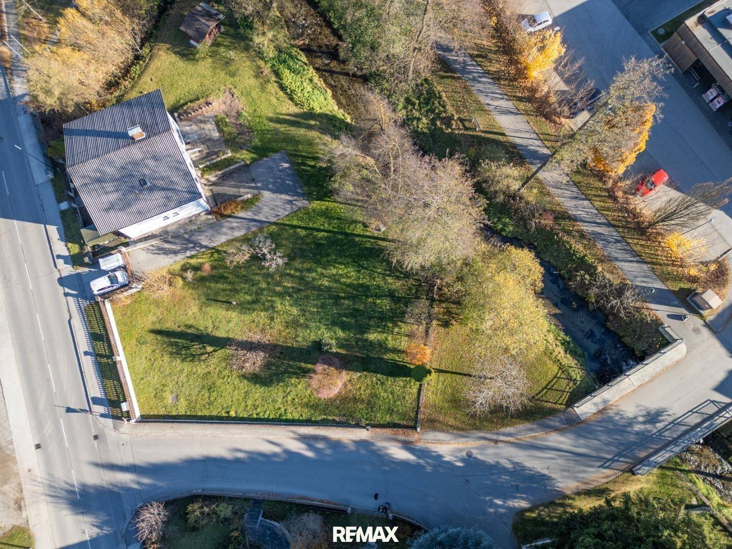 Luftaufnahme eines Hauses mit großem Rasengrundstück, angrenzendem Bachlauf und umliegenden Straßen.