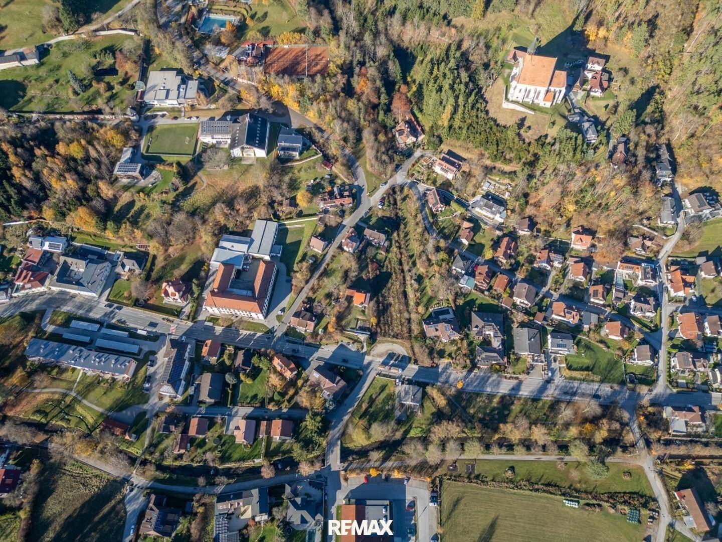 Weitwinkel-Luftaufnahme einer ländlichen Gemeinde mit zahlreichen Häusern, Straßen und einer Kirche auf einem Hügel.