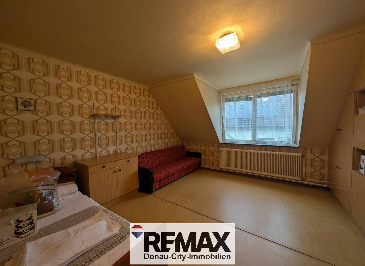 Zimmer im Dachgeschoss mit gemusterter Tapete, Laminatboden, Dachschräge und Sofa.