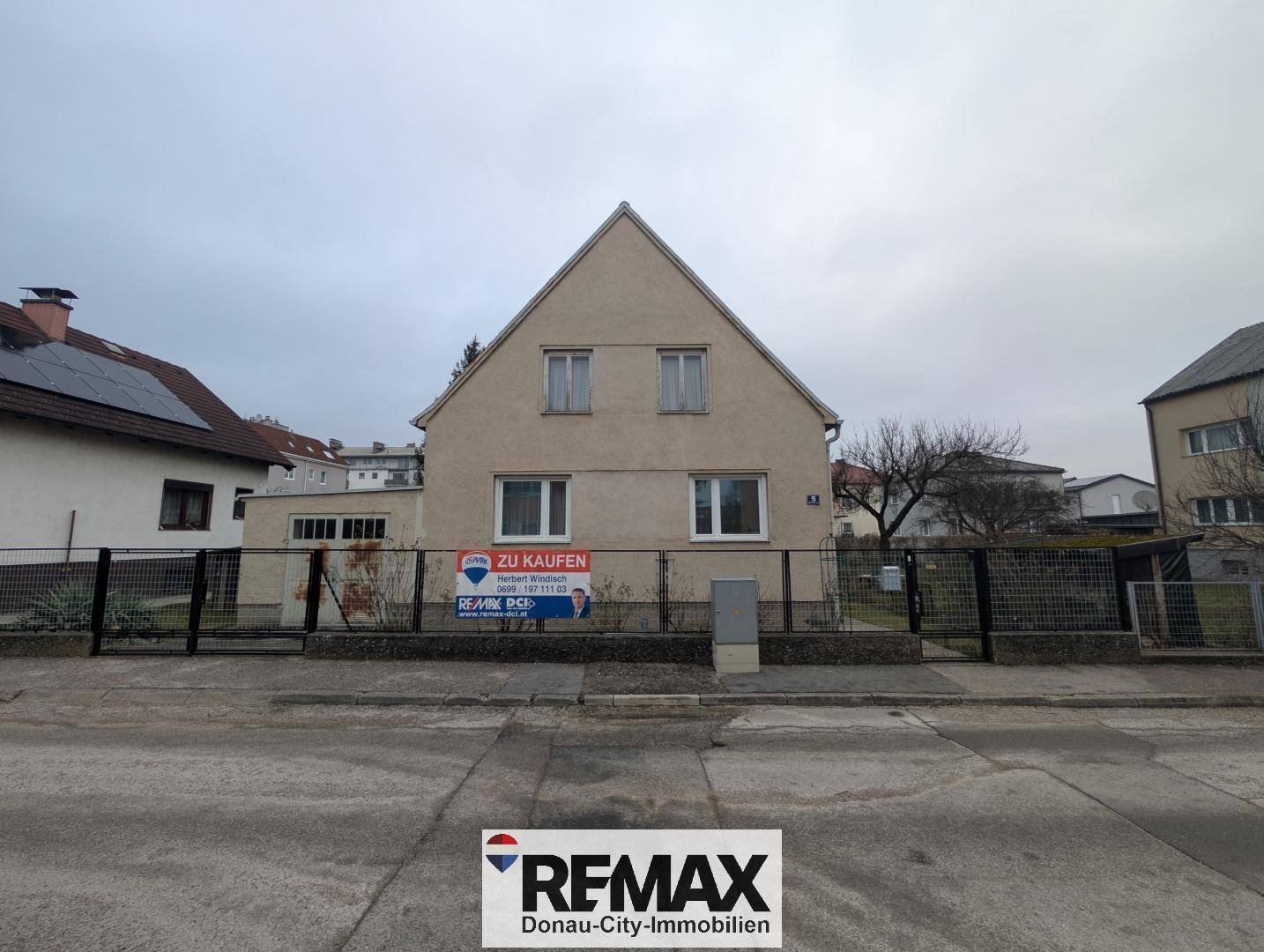 Vorderansicht eines Einfamilienhauses mit Zaun und Schild an einem bewölkten Tag.