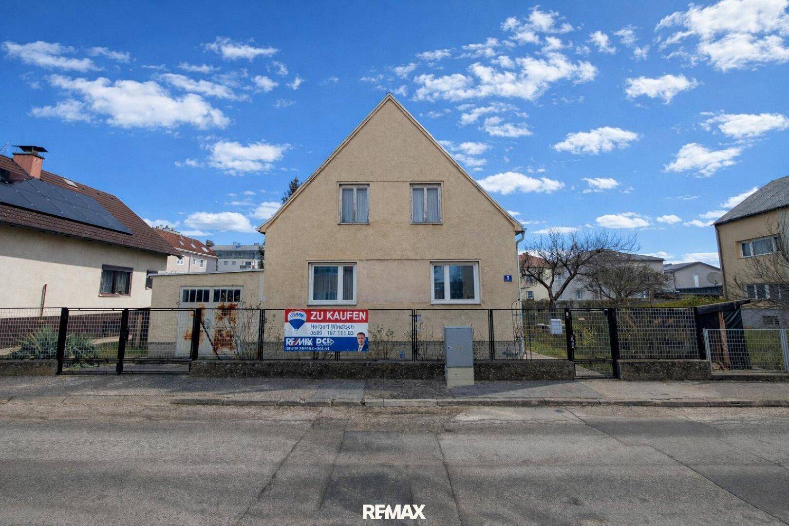 Vorderansicht des Einfamilienhauses an einem sonnigen Tag mit klarem Himmel und 'Zu Kaufen'-Schild.