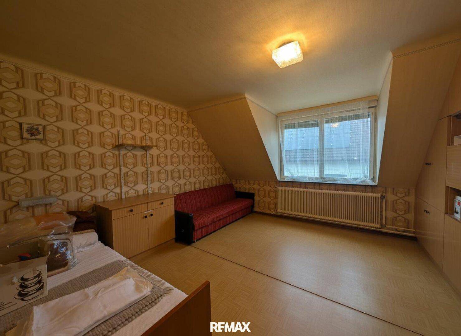 Dachgeschosszimmer mit Bett, Sofa und gemusterter Tapete, ideal als Schlaf- oder Gästezimmer.