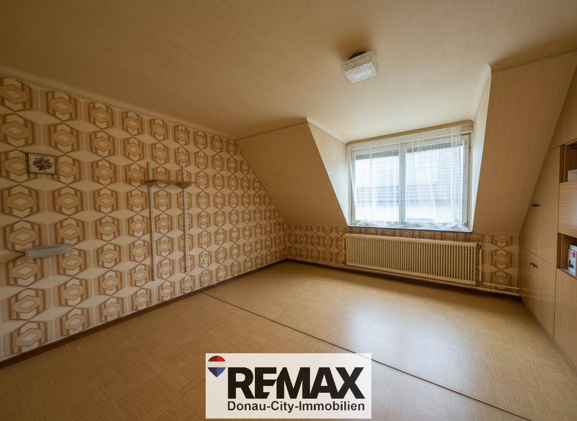 Leeres Zimmer im Dachgeschoss mit gemusterter Tapete, Laminatboden und Dachschräge.