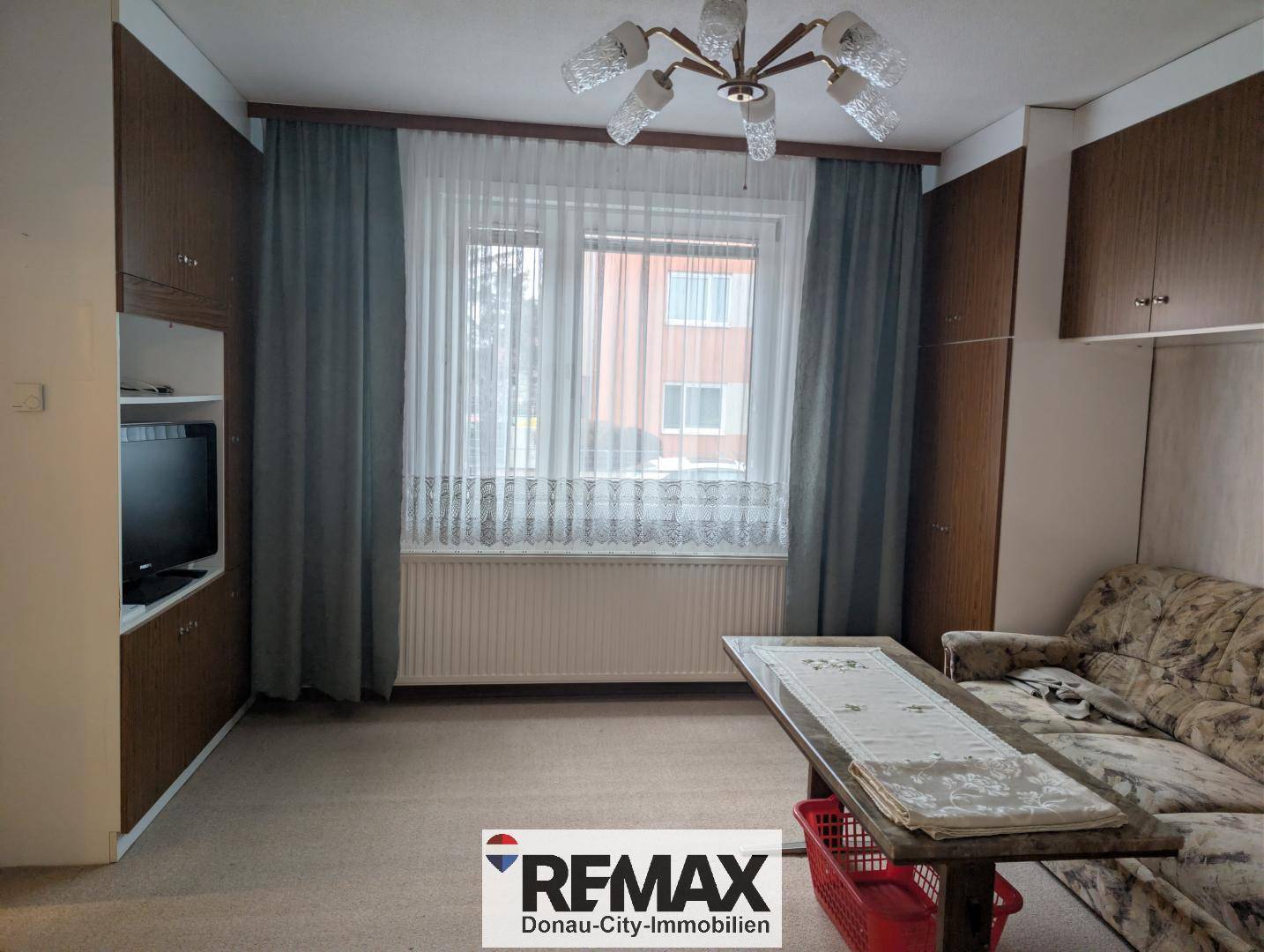 Wohnzimmer mit Teppichboden, Einbauschränken und einem Fenster mit Vorhängen.