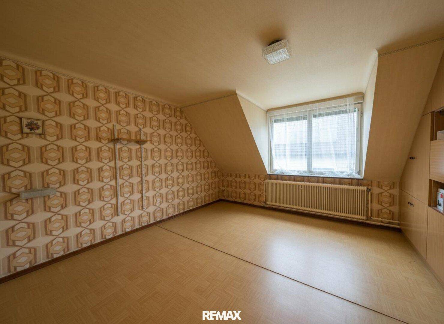 Dachgeschosszimmer mit schräger Decke, gemusterter Tapete und Laminatboden, unmöbliert.