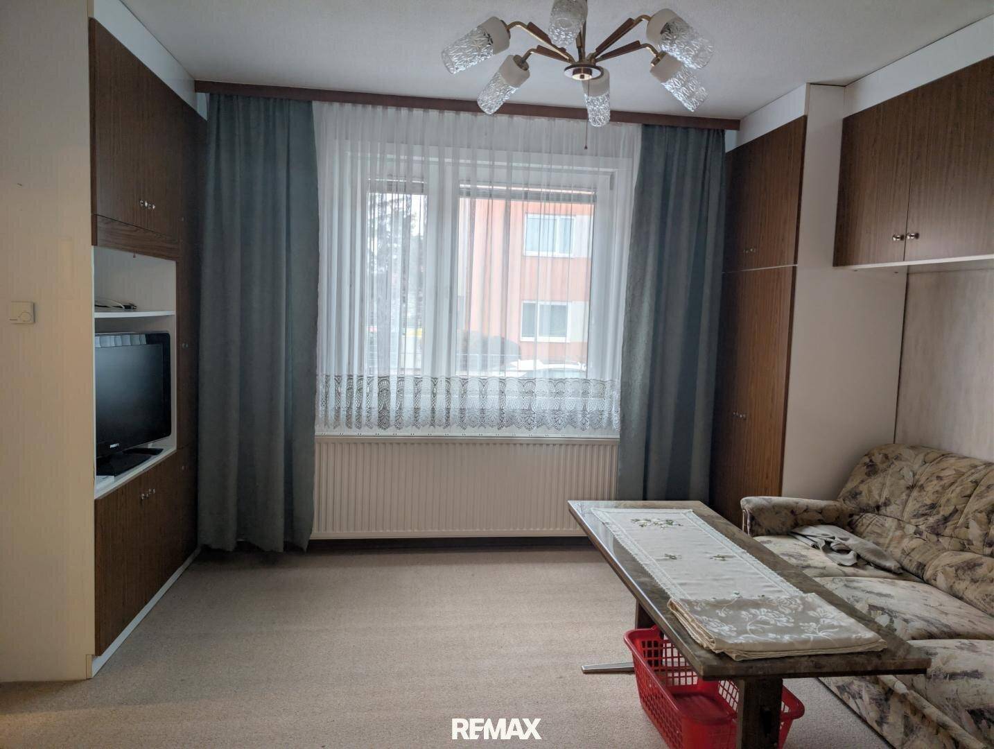 Wohnzimmer mit Teppichboden, Einbauschränken und einem großen Fenster mit Vorhängen.